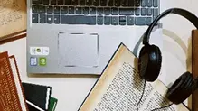 Uma mesa com um notebook, fone de ouvido e caderno de anotações.
